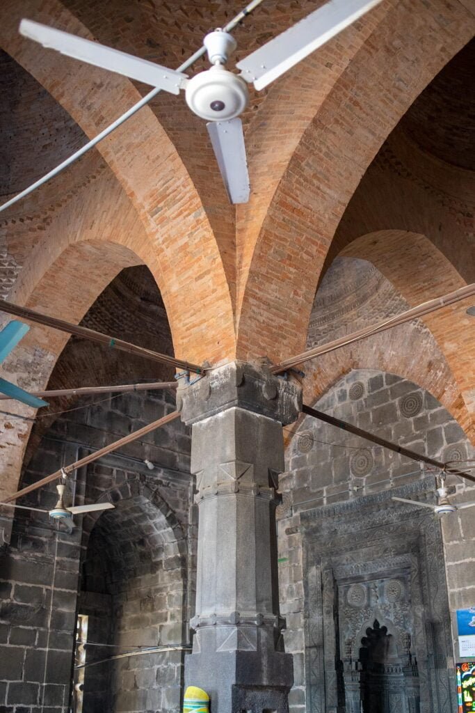 Interior of Kusumba Mosque featuring a stone pillar with brickwork 2023.